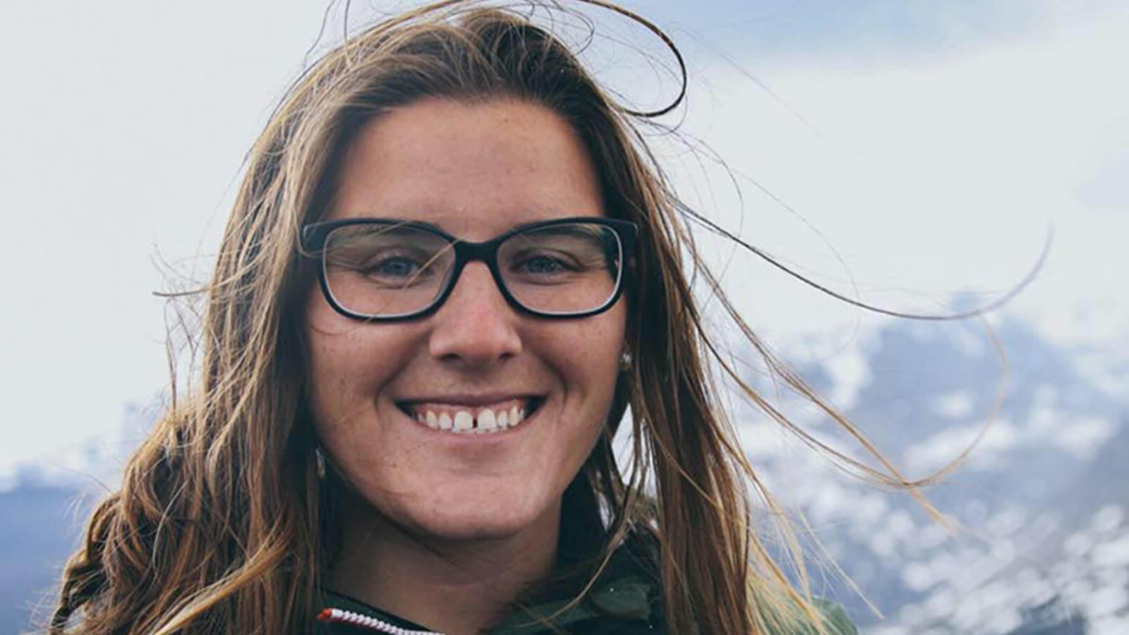Full Sail毕业生SaJorden Miller肩部以上的照片, 背景是白雪皑皑的山脉. 她面带微笑，穿着一件橙色的绿色拉链夹克，戴着一副黑框眼镜.