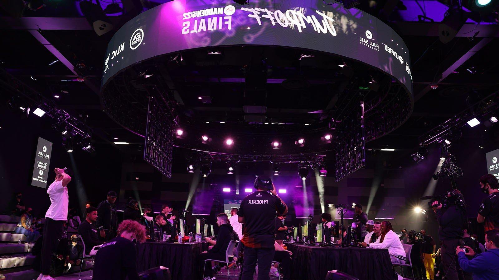 The 满帆大学 Orlando Health Fortress esports arena’s main stage and large screens feature Jump Off’s purple and white branding while competitors face-off at gaming stations.