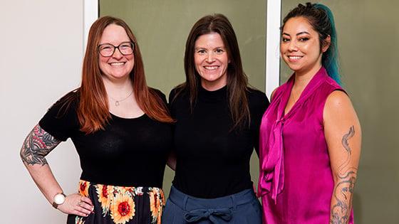 三位来自《十大菠菜台子》的女性获得了今年的游戏奖提名，她们站在一起，对着镜头微笑.