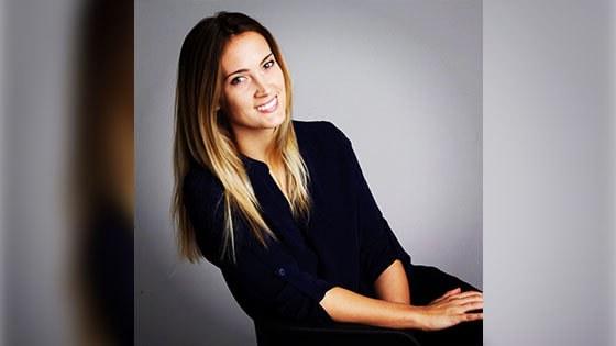 Grad Lisa Maskey, a smiling woman with straight blond hair wearing a black three-quarter sleeve top seated against a grey backdrop.