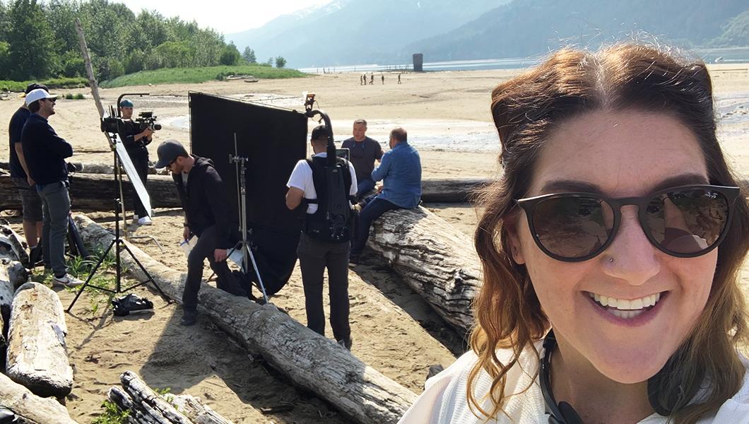 Jenn Miller stands on a beach in Juneau, Alaska. A film crew sets up lighting equipment behind her.