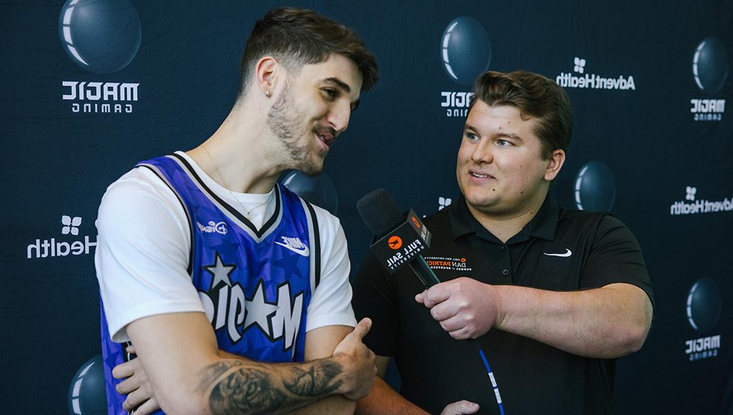 一个人在采访一个穿着奥兰多魔术队篮球球衣的人时，拿着一个标有满帆的麦克风.